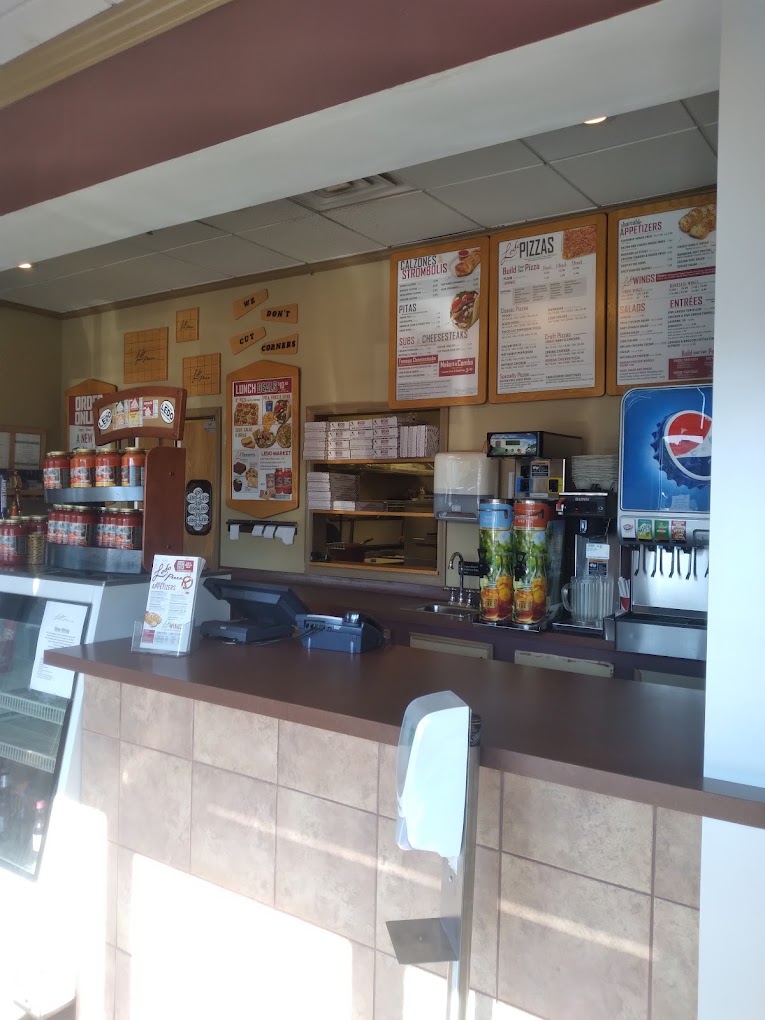 A casual fast-food restaurant counter with menu boards, a register area, and beverage dispensers, photographed from the customer's perspective.