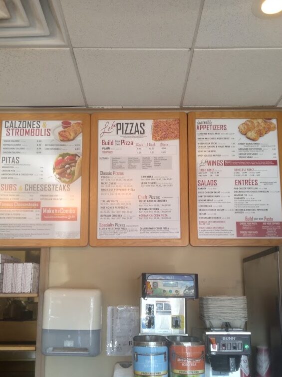 A fast-casual restaurant counter displaying menu boards on the wall above beverage dispensers and a coffee machine.