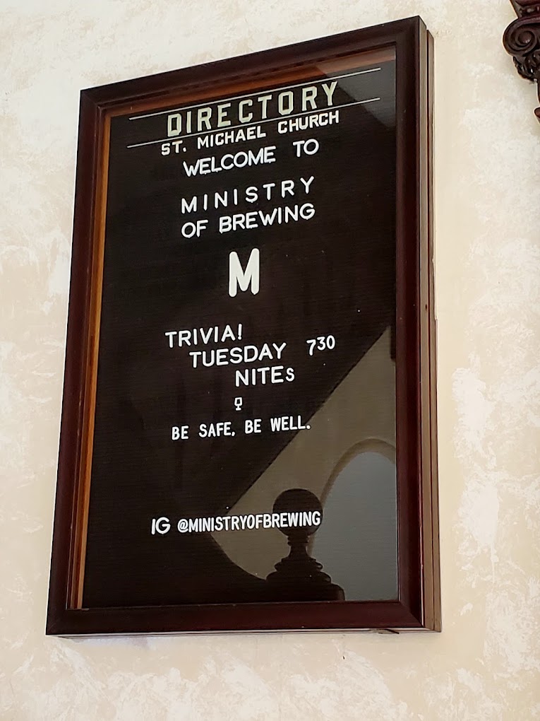 A framed directory sign for a Ministry of Pruning venue displays service times and contact information on a white background with black text.