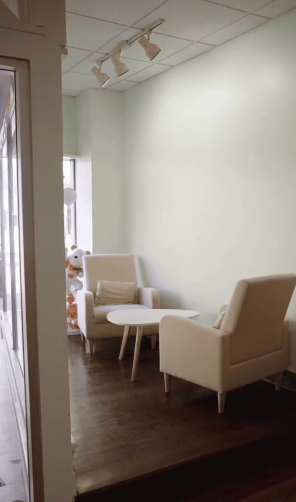 A cozy indoor sitting area with two beige armchairs and a small round table on a wooden floor.