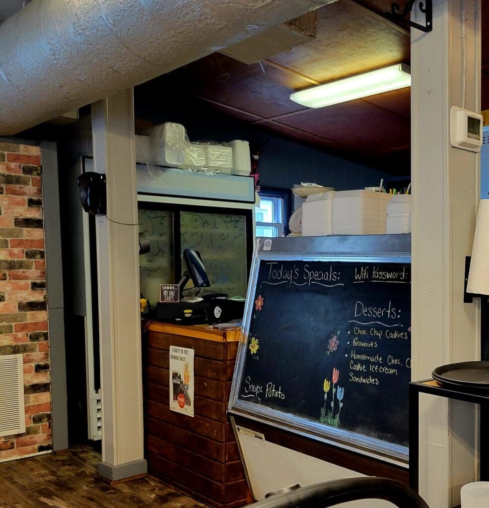 An organized workshop or studio space with exposed brick walls, shelving, a chalkboard menu or notes, and computer equipment under warm lighting.
