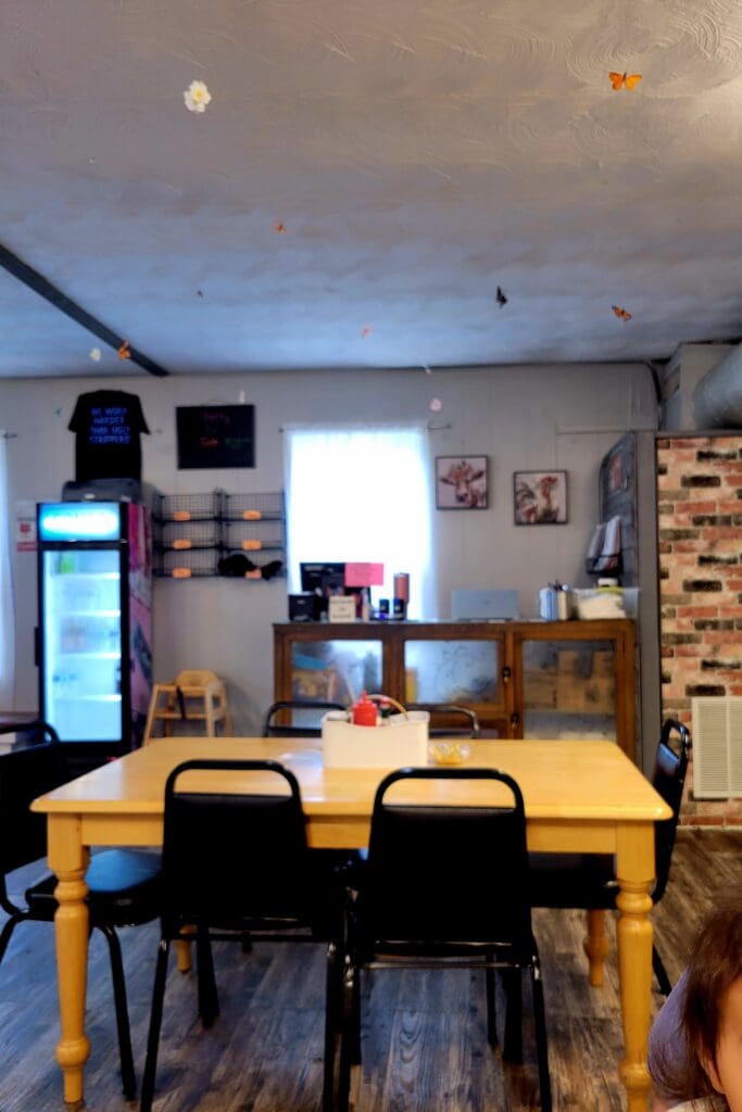 An indoor kitchen or dining space with a wooden table, black chairs, brick wall accents, and shelving along the walls in warm lighting.