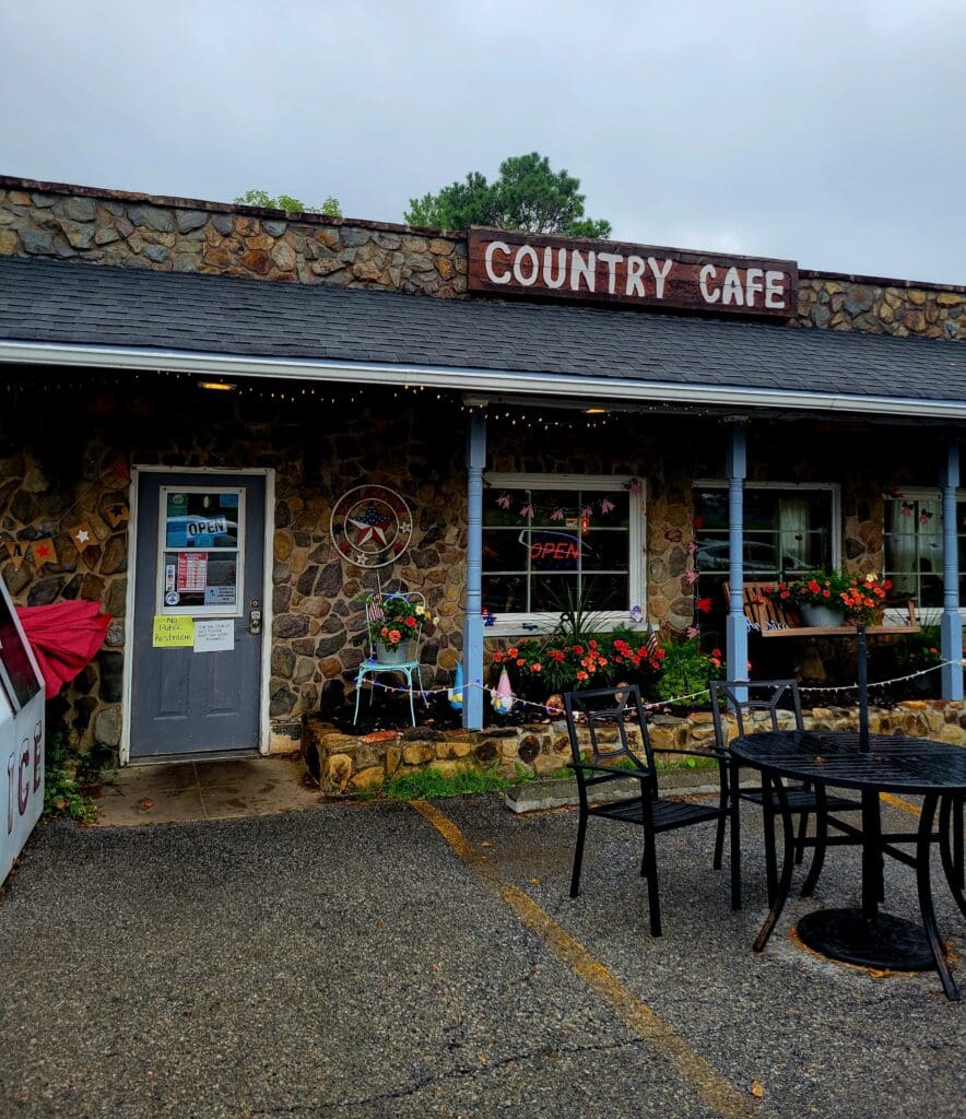 A charming country cafe with rustic charm features outdoor seating with flowers and weathered wooden signage.