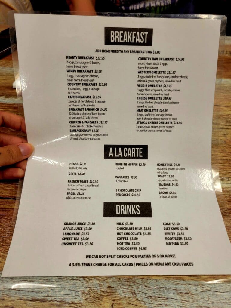 A person holds an open restaurant menu displaying breakfast items and drinks at a dining establishment.