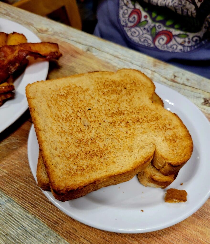 A close-up shot of cinnamon-sugar toast and crispy bacon arranged on a white plate, captured indoors.
