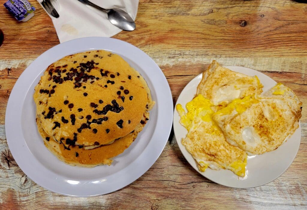 Two freshly baked pastries served on white plates on a wooden table, featuring a chocolate-topped pastry and a folded pastry with melted cheese or butter.