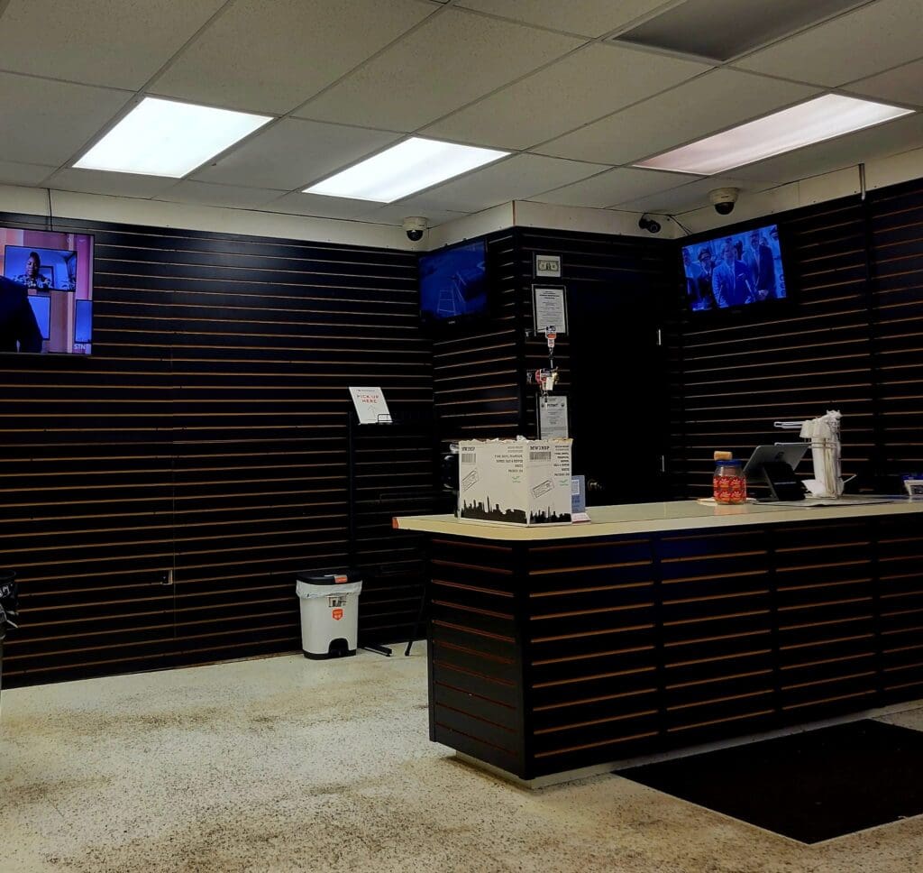 An empty retail or food service counter with black slatwall paneling, blue monitor displays, and fluorescent ceiling lighting.