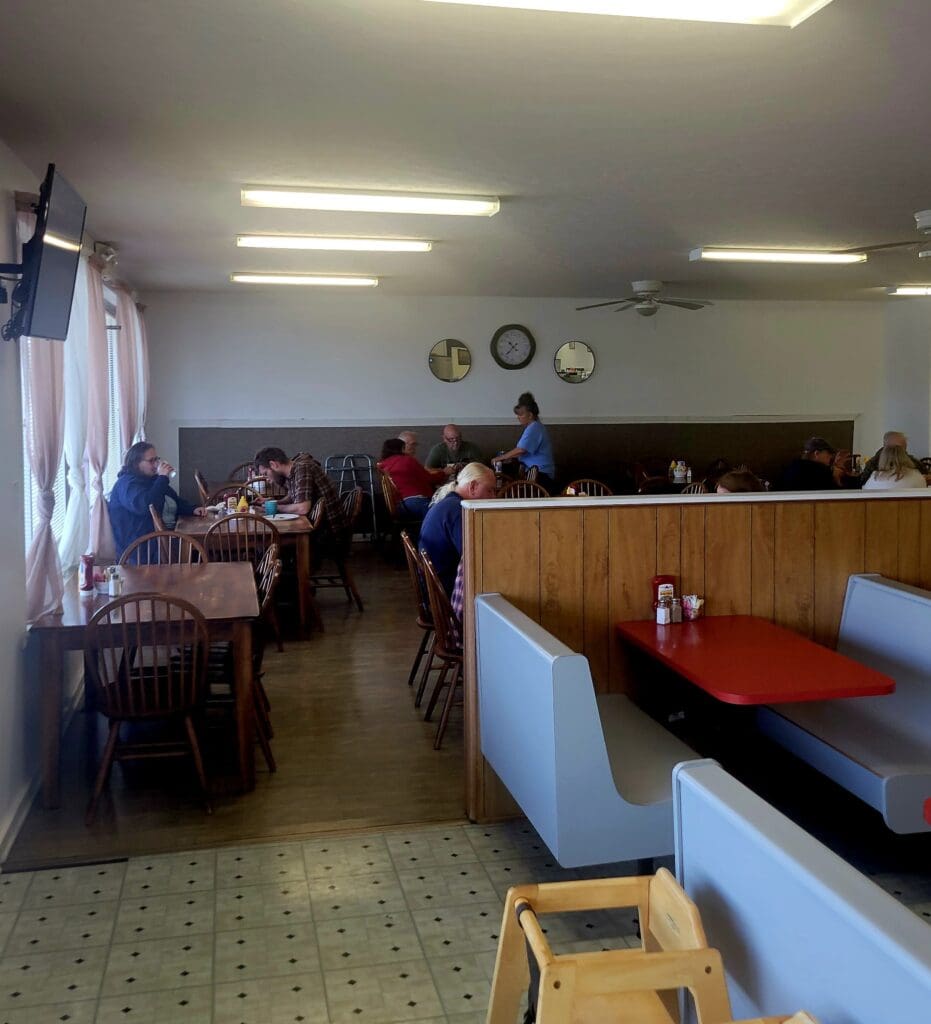 A casual diner or restaurant interior with wooden tables, a red booth, and several people seated and eating.