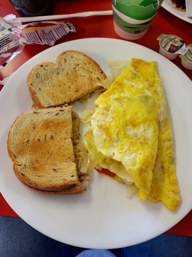 An overhead view of a breakfast plate with a folded cheese omelette and toasted rye bread, accompanied by coffee and creamer cups on a red diner table.