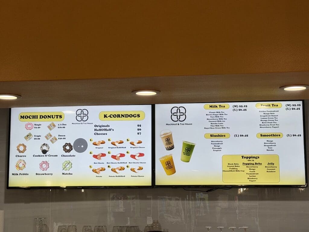 Two digital menu screens display a food shop's offerings including mochi donuts, Korean corndogs, milk tea, fruit tea, slushies, and smoothies.