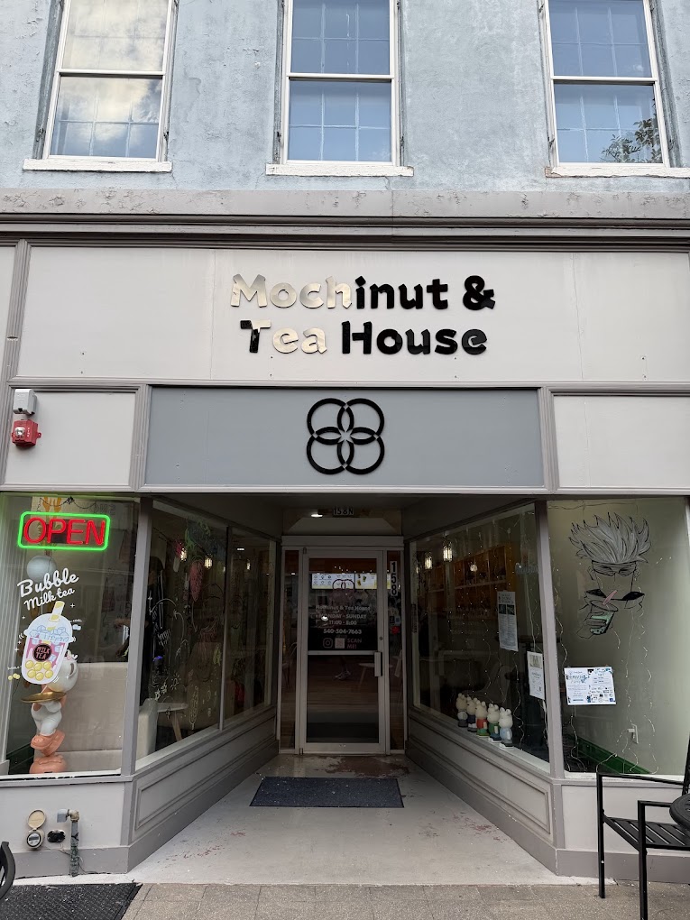 Exterior storefront of a shop called Mochinut & Tea House with a neon 'open' sign and bubble tea artwork on the windows.